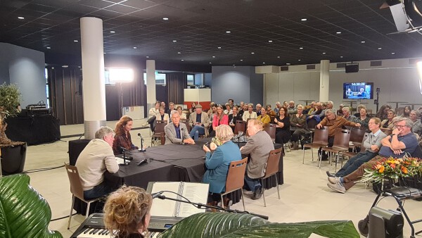 Overzichtsfoto symposium streektaal in de zorg met gespreksleider Frans Miggelbrink, tafelgasten en publiek.